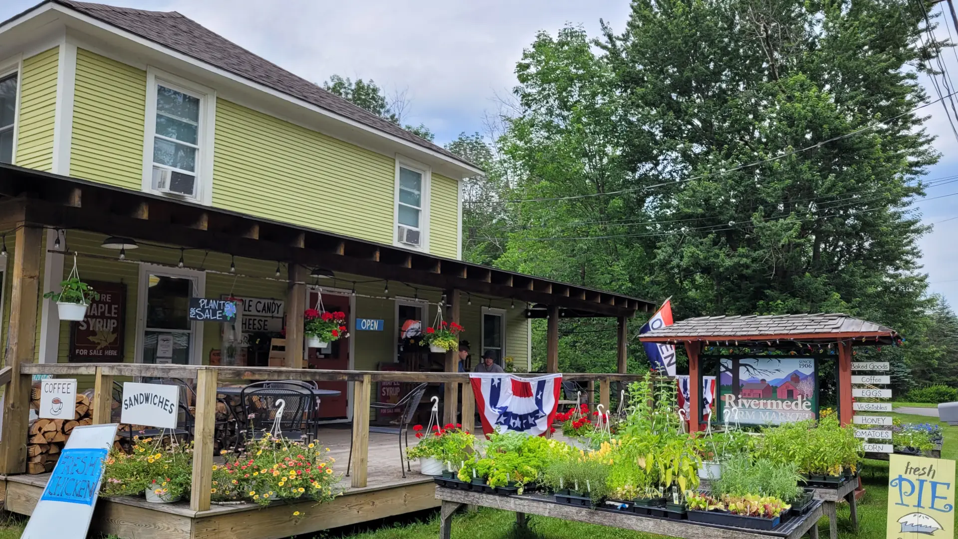 Rivermede Farm Market is a yellow building with a big front porch. Two men and their dog are on the front porch