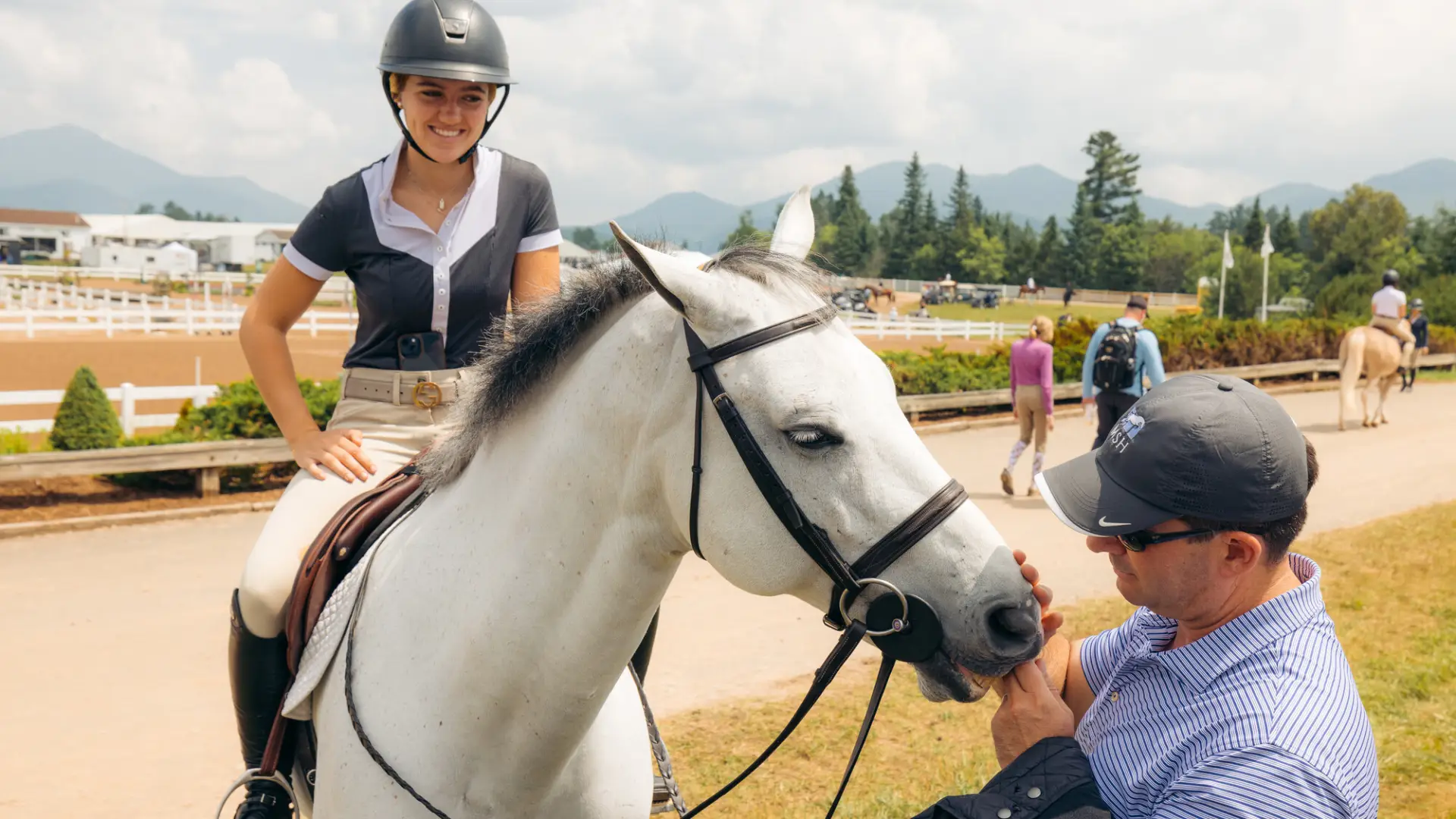 A rider, her horse, and person petting her horse.