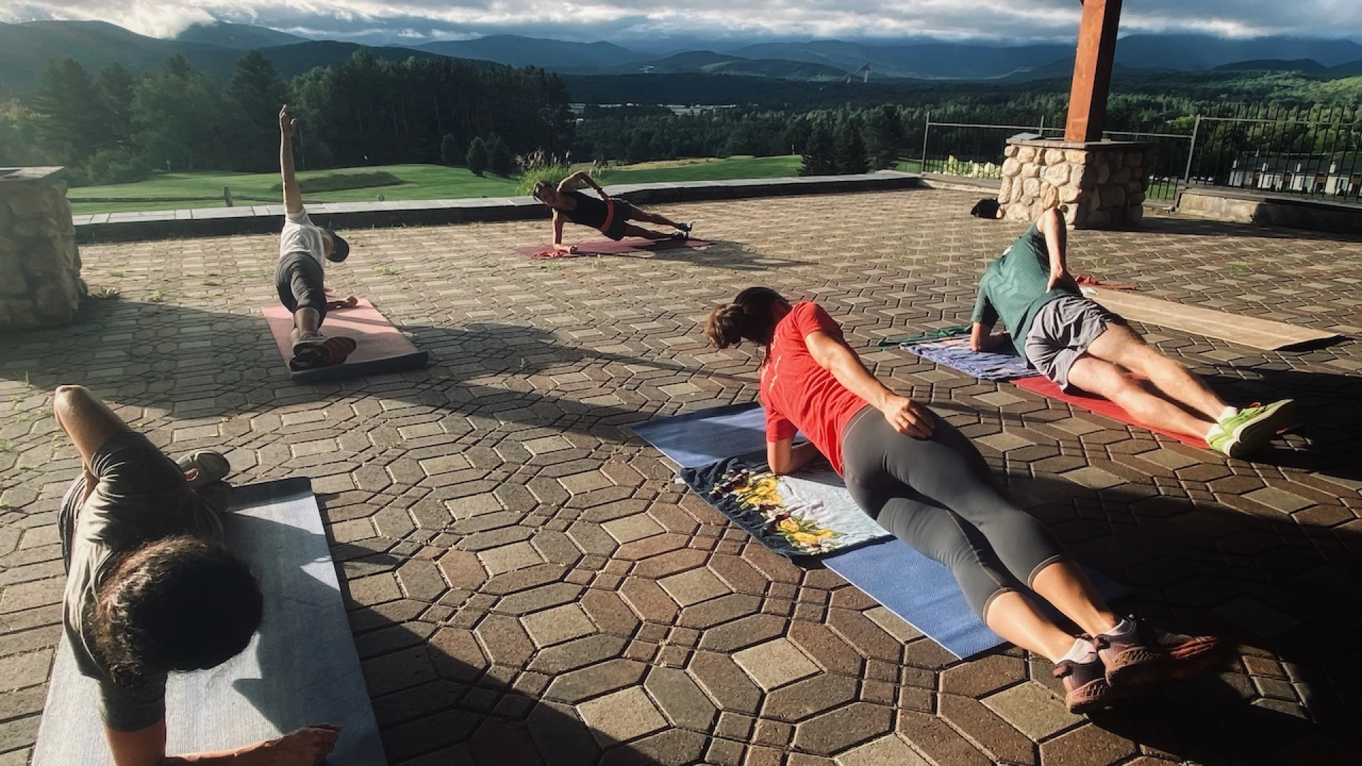 People prop themselves on one elbow with their legs extended in a side plank on yoga mats on covered brick patio