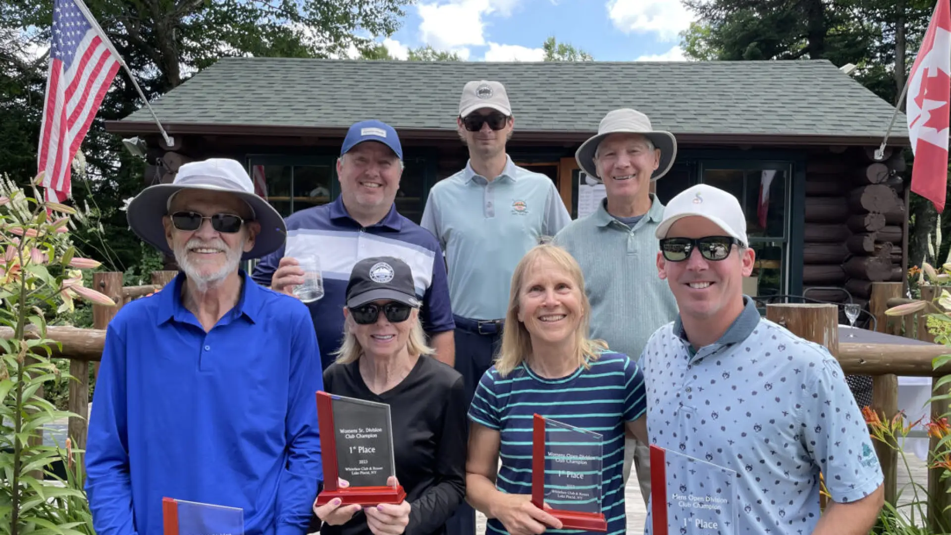 Seven people stand in two rows posing with glass awards from golf tournament outside on a summer day
