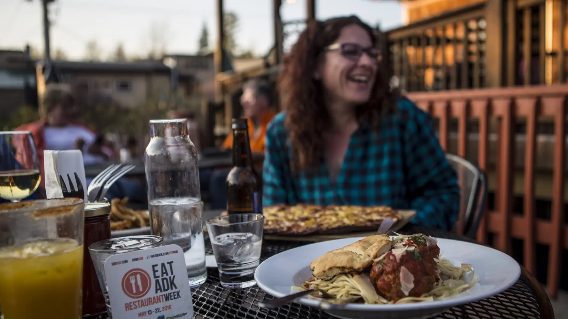 A woman laughs with food on a patio.