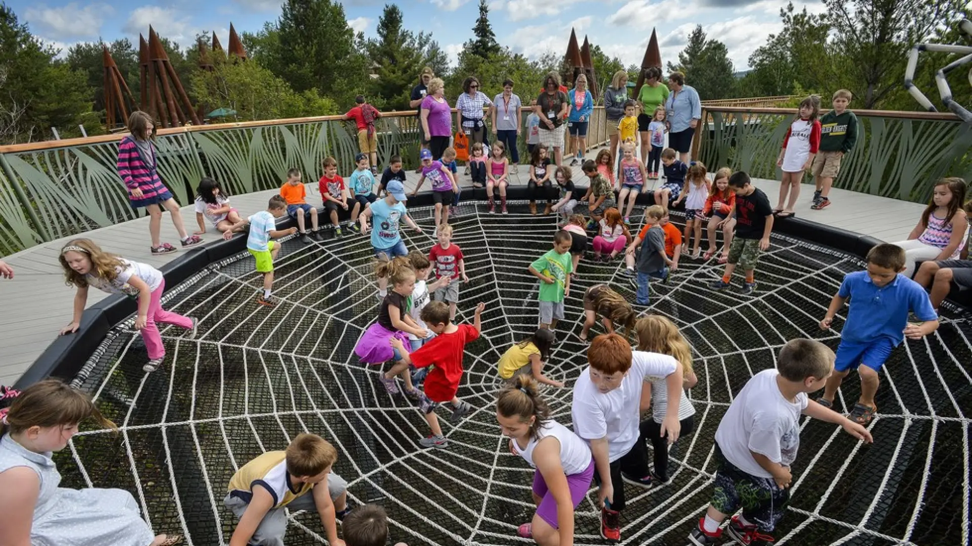 Dozens of children playing on the outdoor spiderweb exhibit