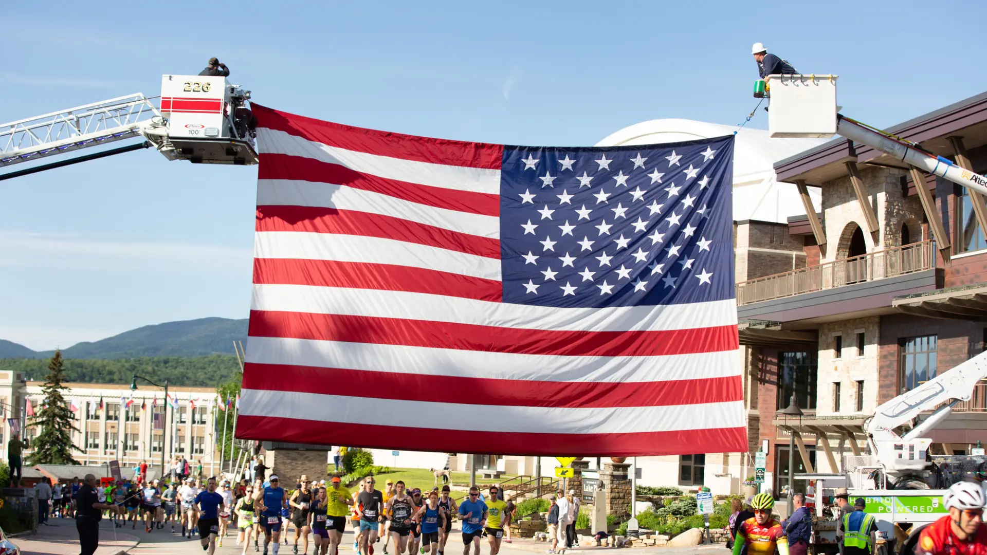 Two cranes hold up a large American flag over a marathon route through town.