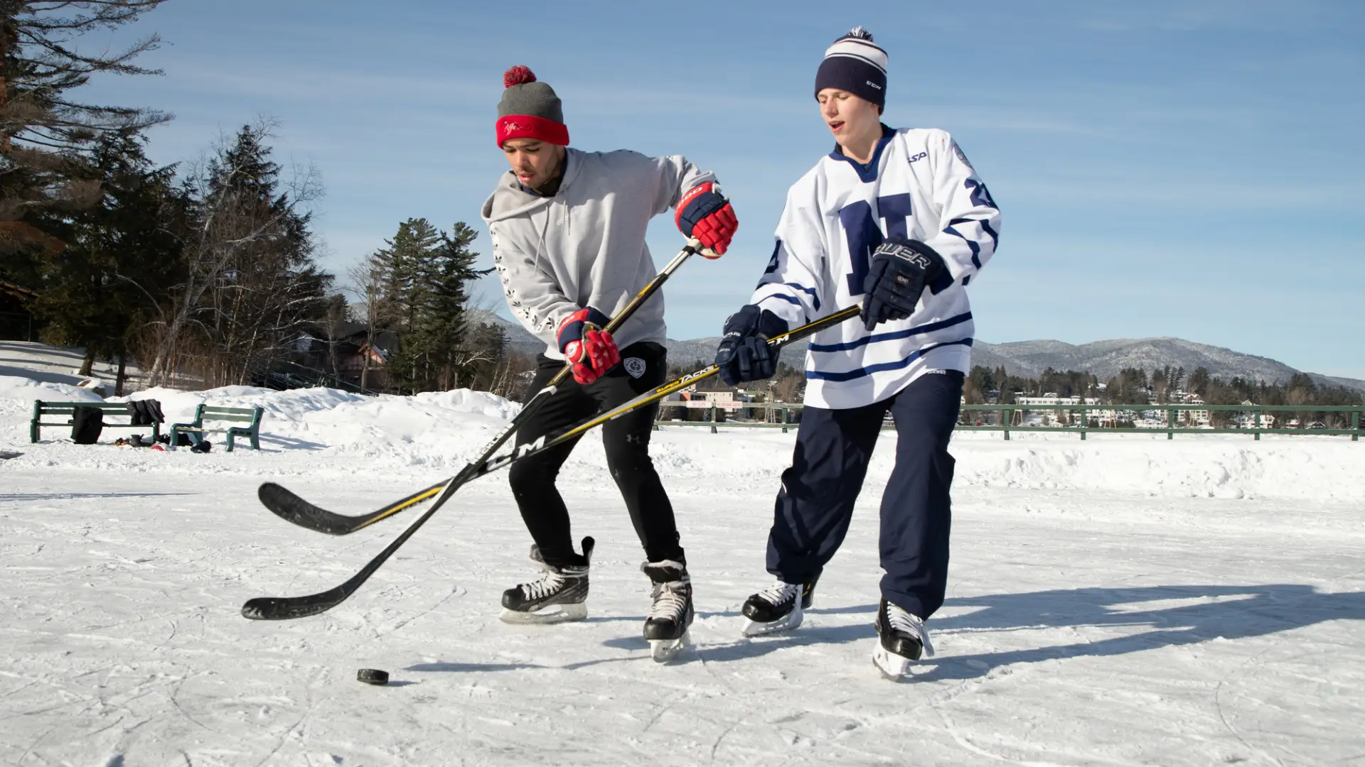 Two kids play ice hockey on a frozen lake