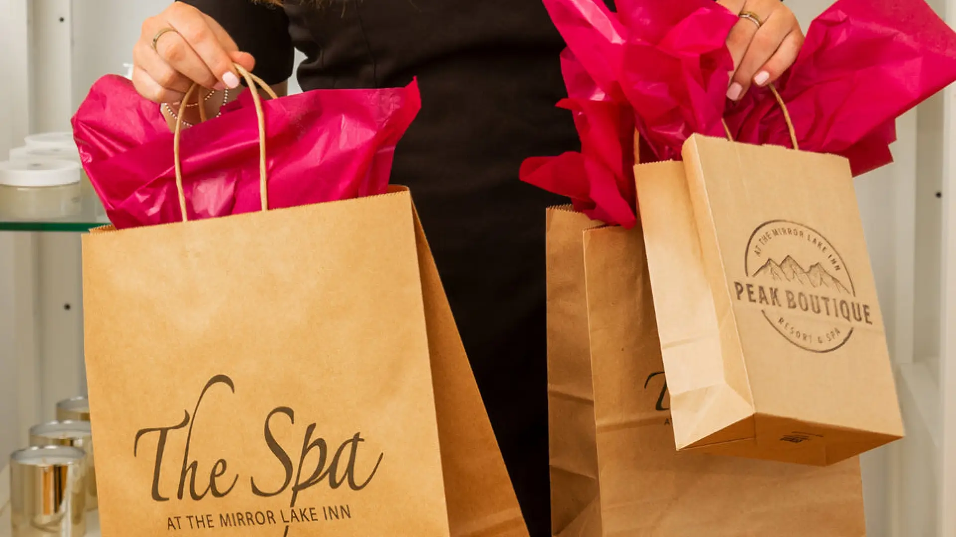 A smiling woman holds multiple sized paper bags with handles and tissue paper from The Spa at Mirror Lake Inn Resort.