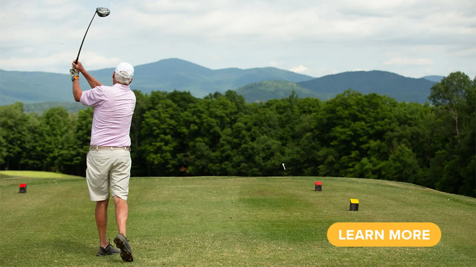 A golfer tees off toward the Adirondack Mountains.