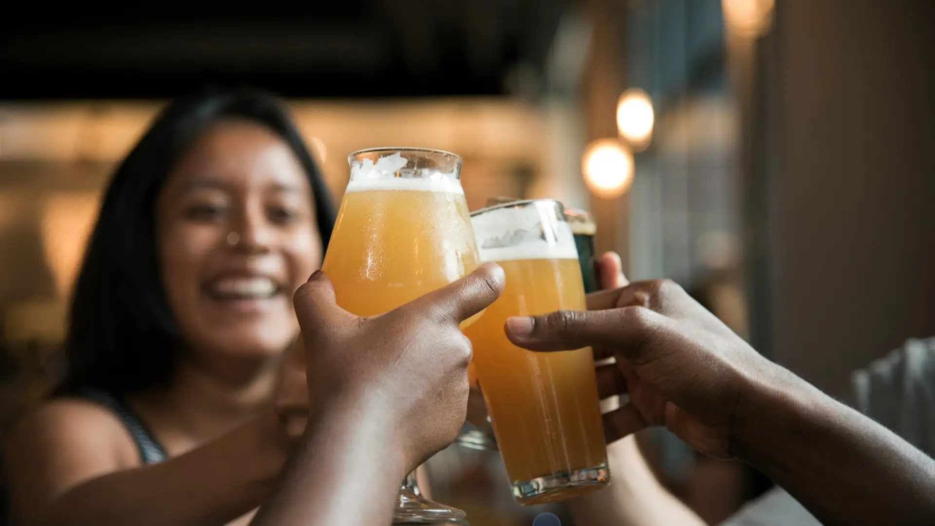 Stock image of woman raising glass of beer smiling and arms from people off screen also raising arms in cheers