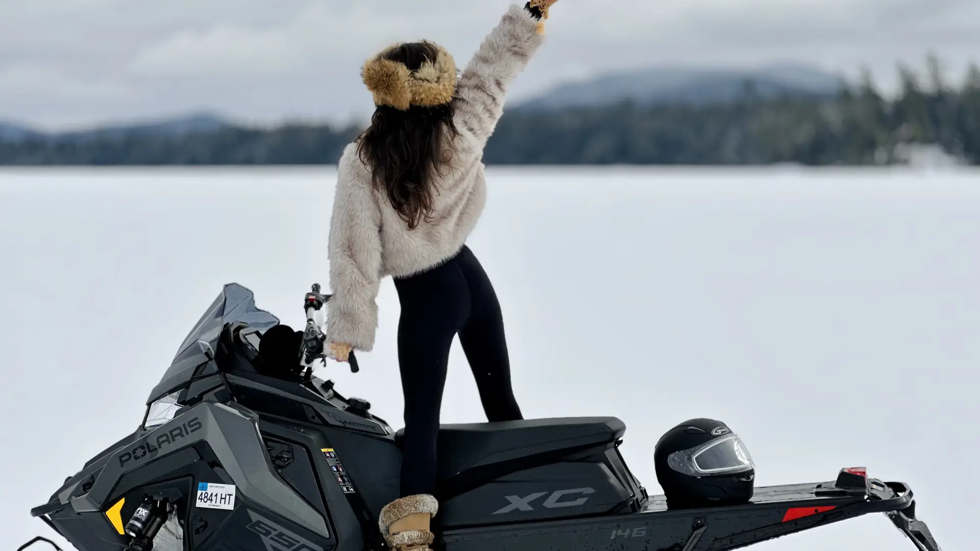 excited girl in furs looks out over the snowy landscape from atop a polaris snowmachinewith mountain backdrop