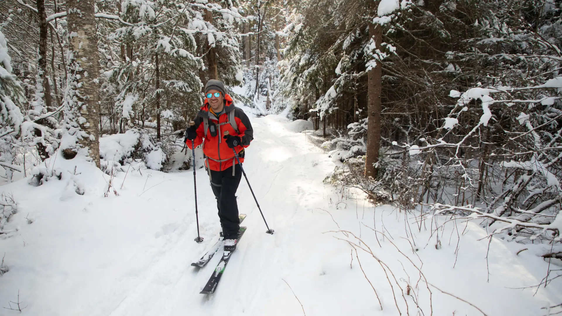 A man smiles as he cross-country skis through a snowy trail.