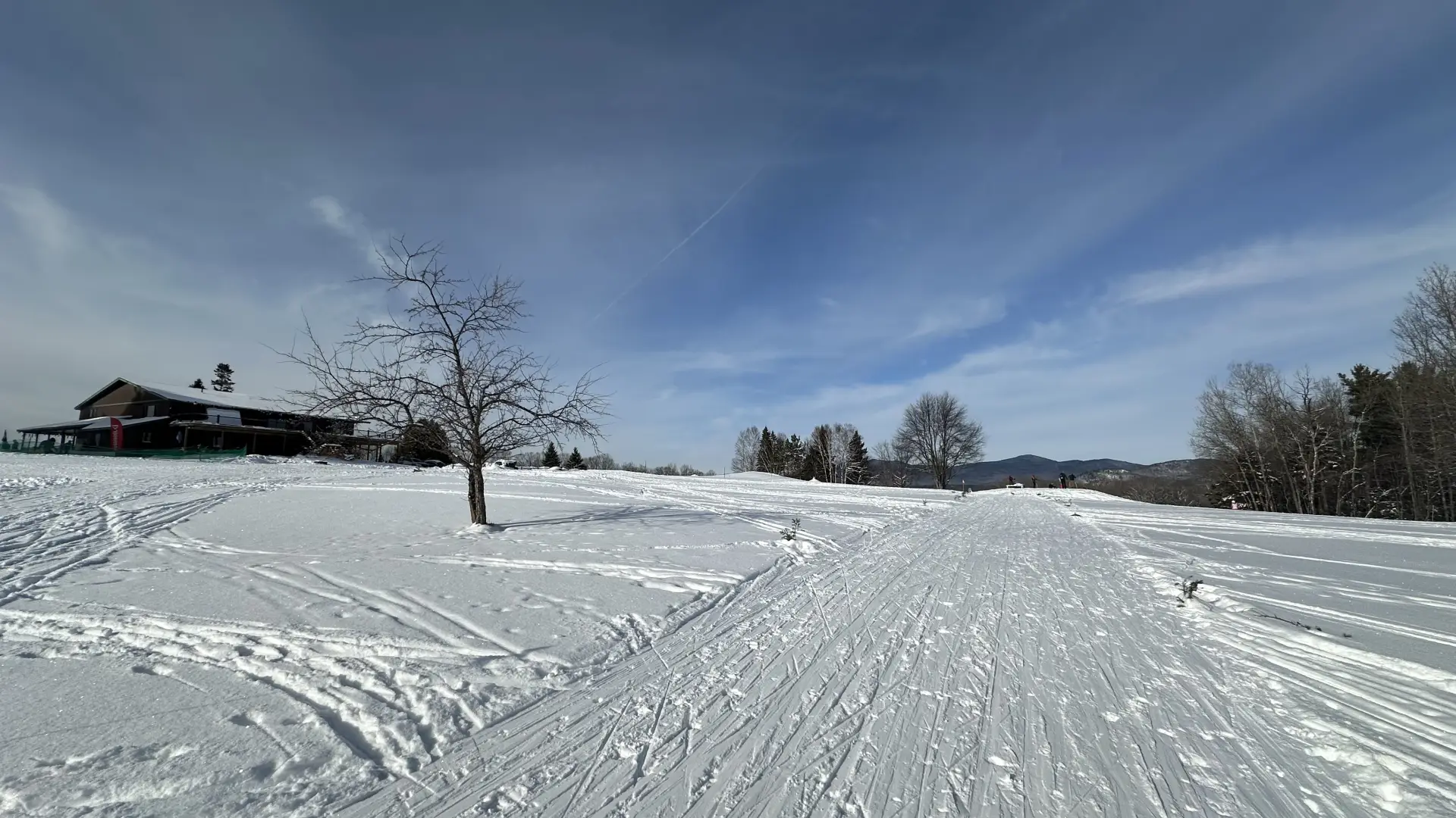 Image of wide cross-country trail over open golf course terrain with lodge seen in the lefthand side