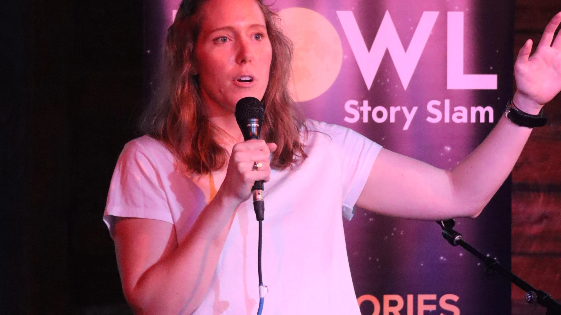 woman stands holding hand up speaking into microphone