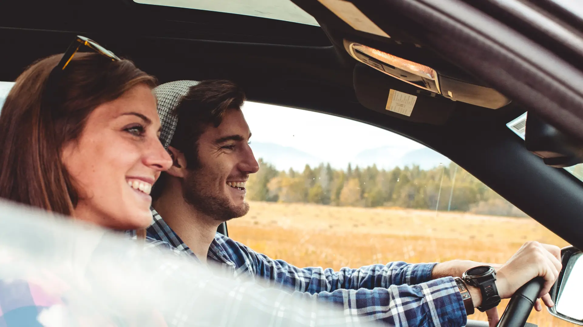 A couple driving a car with a scenic background behind them.