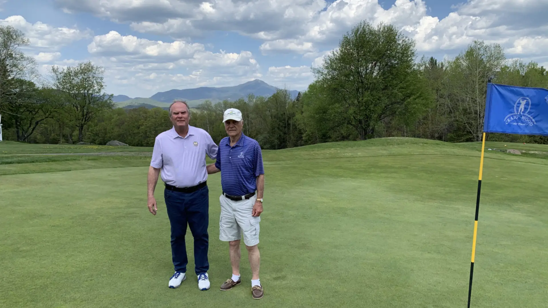 Craig Wood golf pro Jeff Estes and staff member Dick Strack pose on a green with Adirondacks in the background.