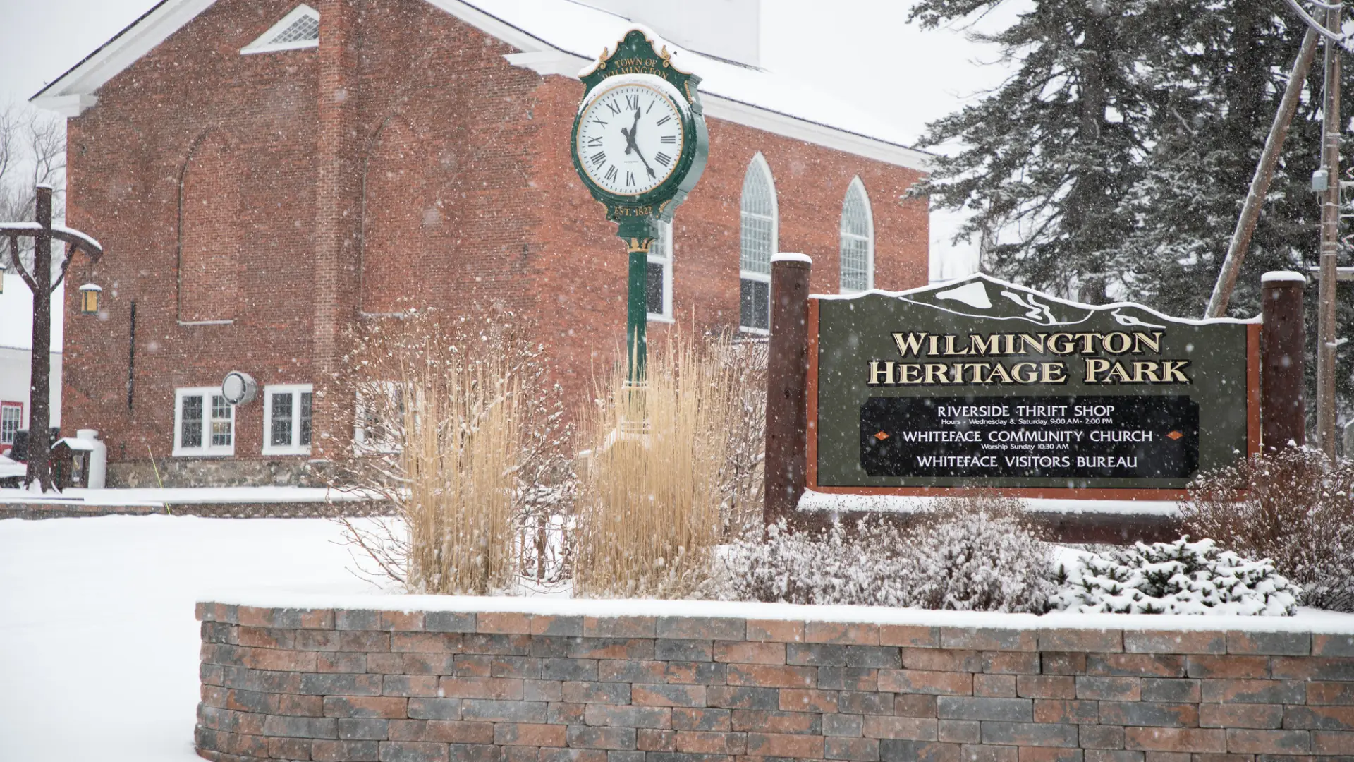A church in the snow with a Wilmington Heritage Park sign in front of it. 