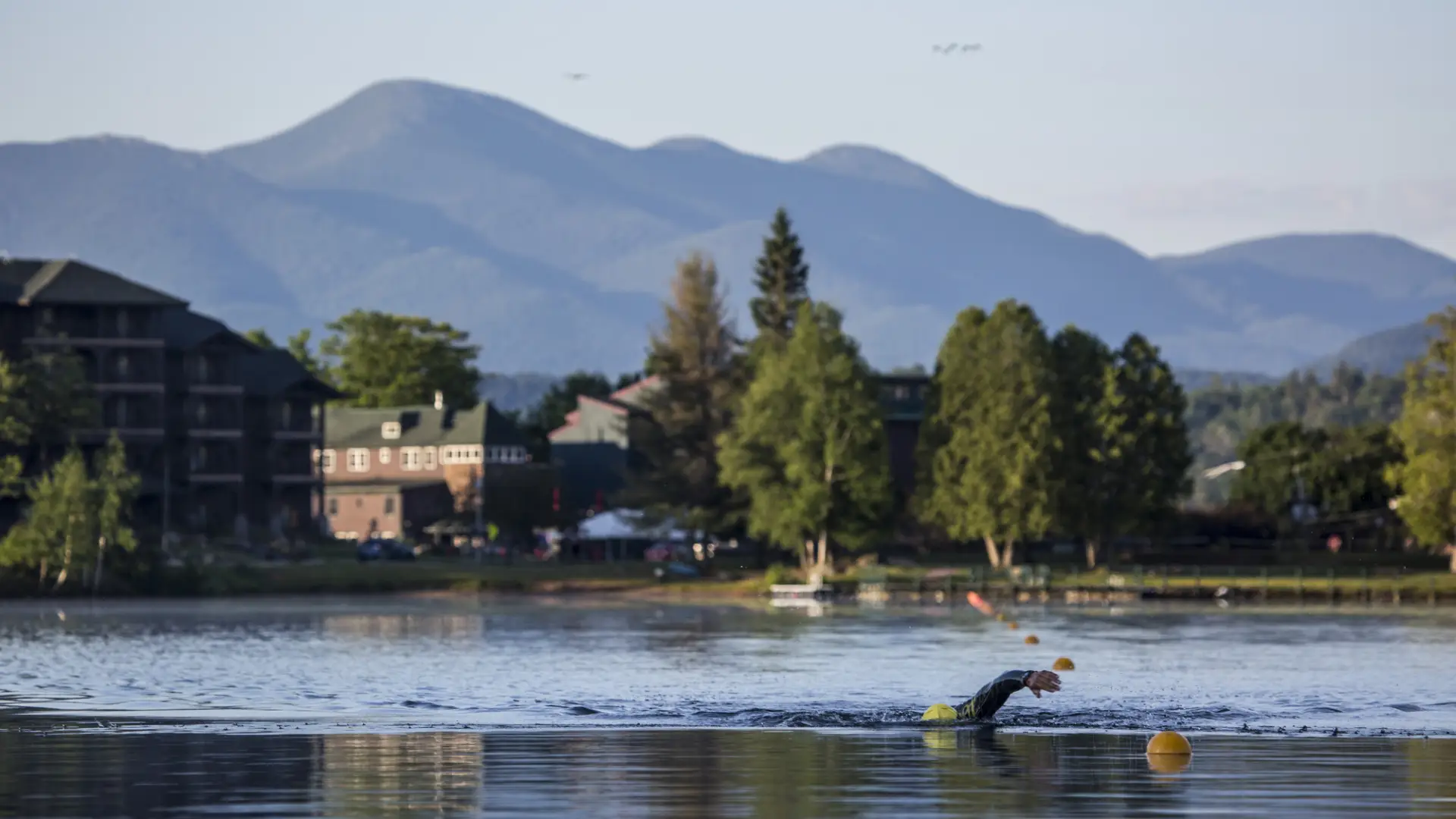 A person swimming in the lake with mountains in the background.