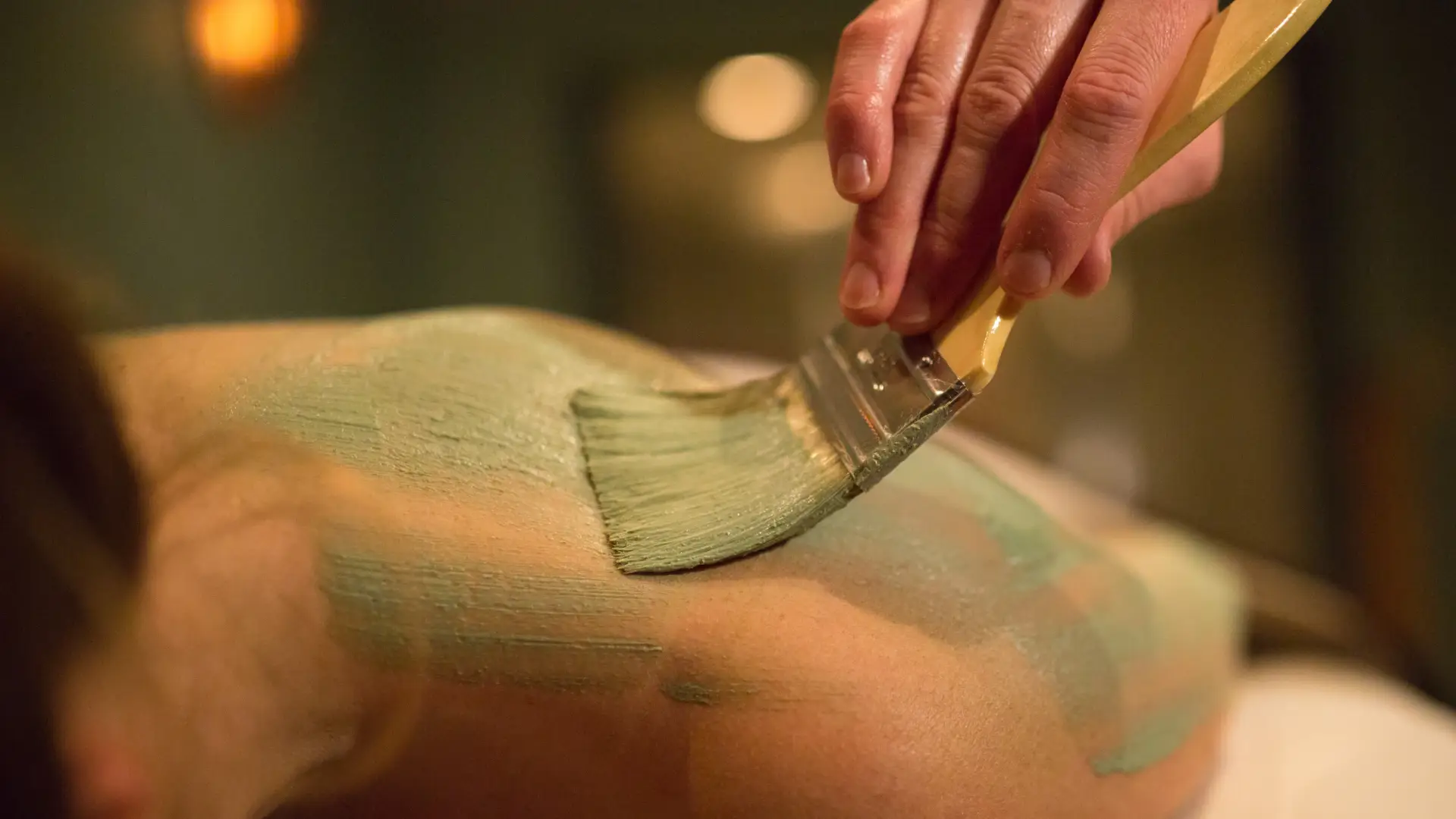 Person paints a green salve onto a persons shoulders with a paint brush