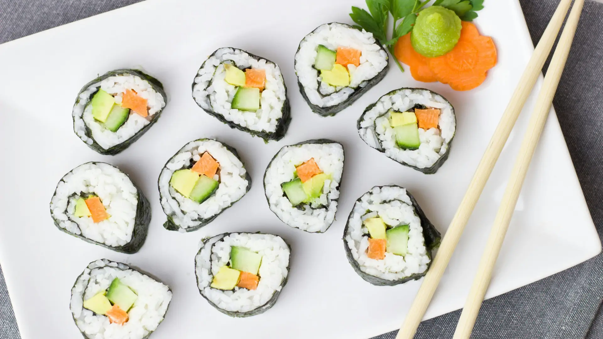 White rectangular plate with sushi rounds accompanied by side of ginger and wasabi.