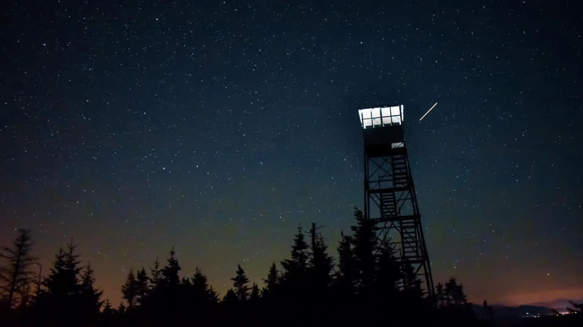 Silhouette of a fire tower at night under a starry sky with a shooting star.