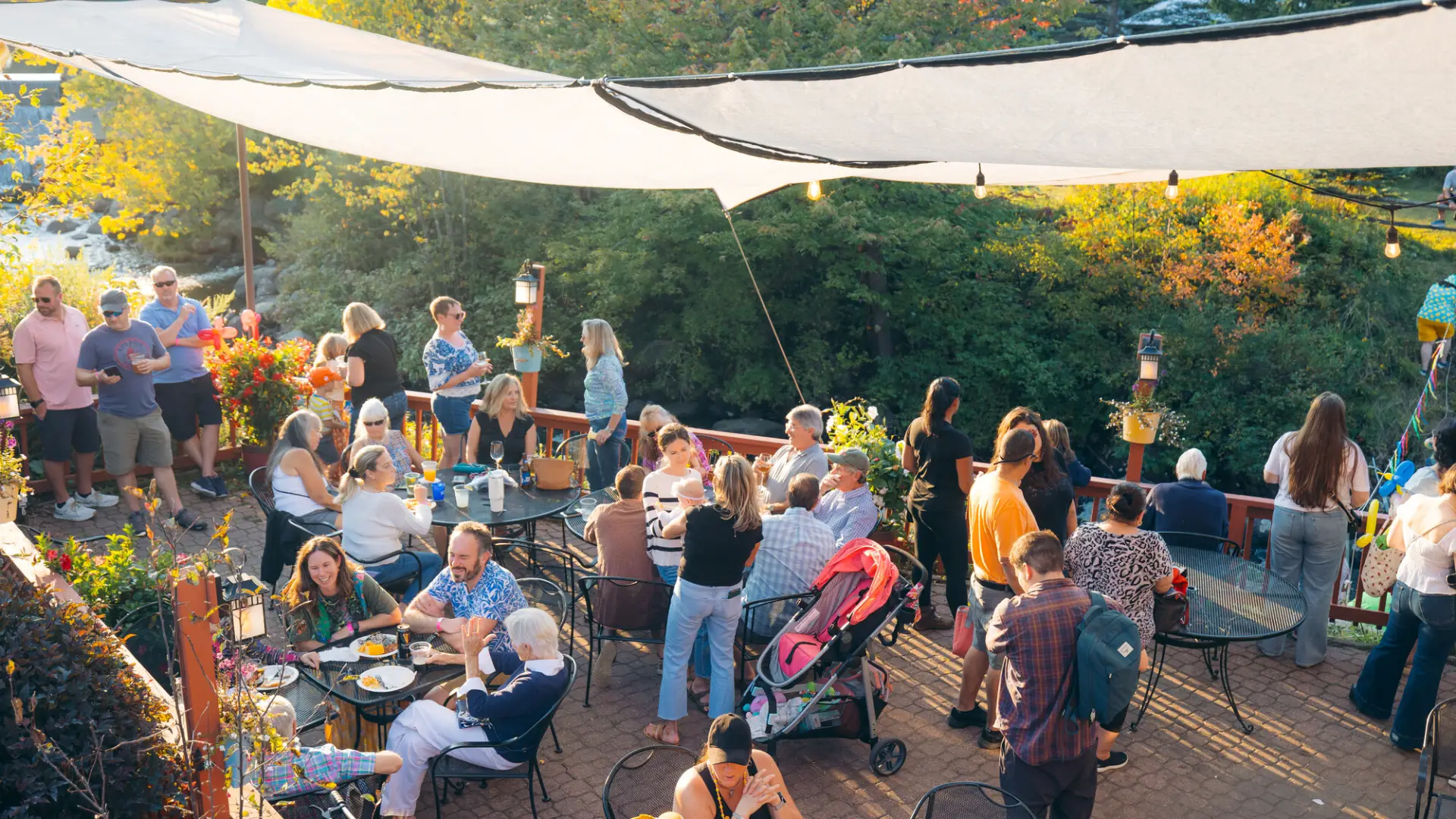Crowd photographed from above on canopied outdoor patio sitting at tables and standing, some wearing duck accessories 