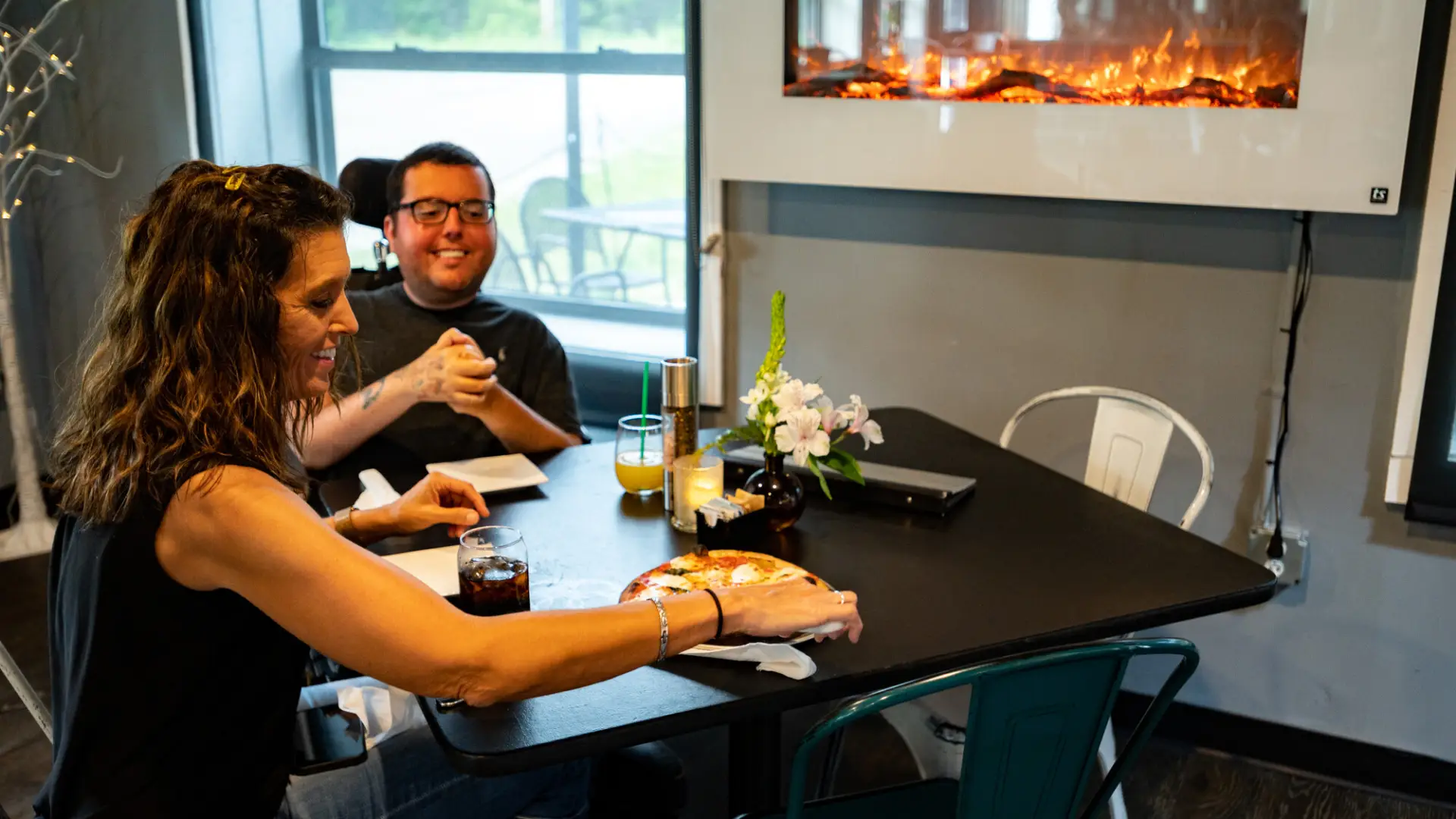 A woman and a man in a wheelchair eating pizza at a table.