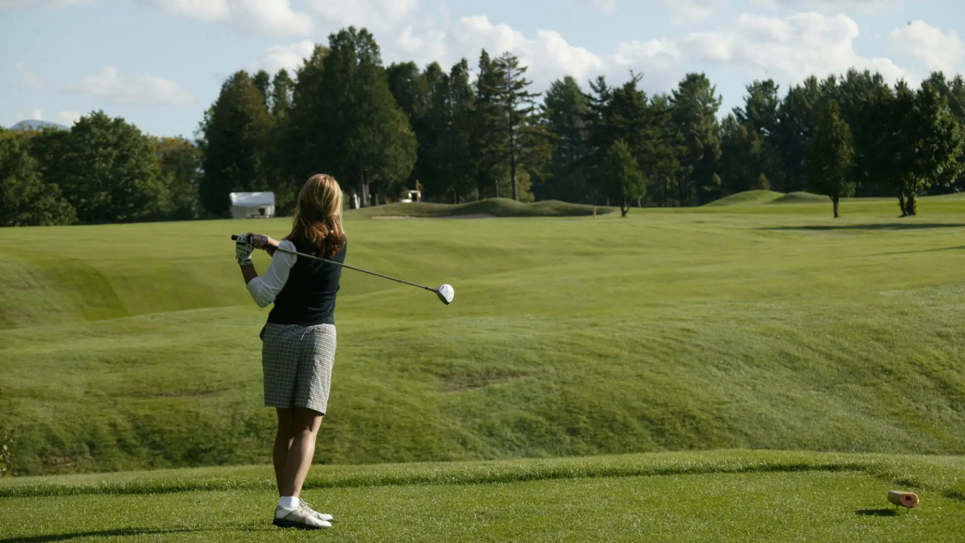 Woman in golf attire stands in backswing with golf club on green of Whiteface Club & Resort golf course