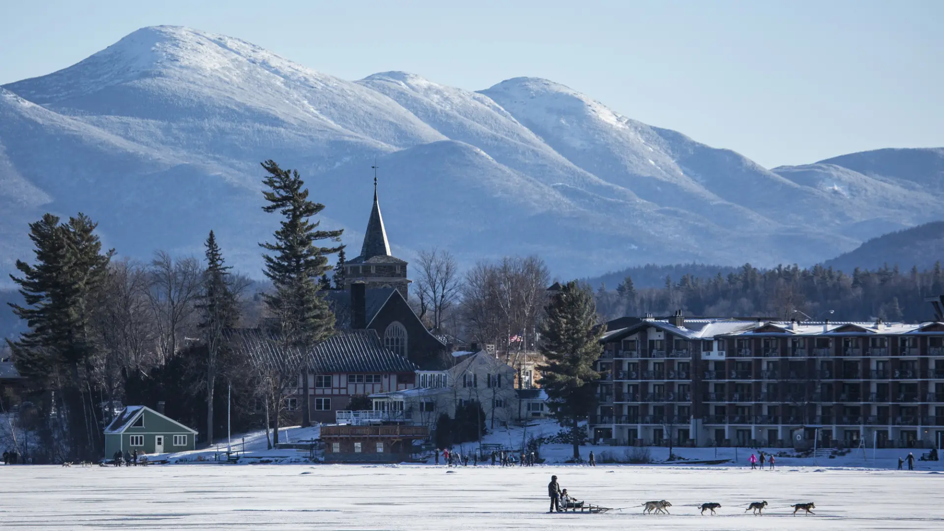An aerial shot of mirror lake with dog sledding and winter mountains.