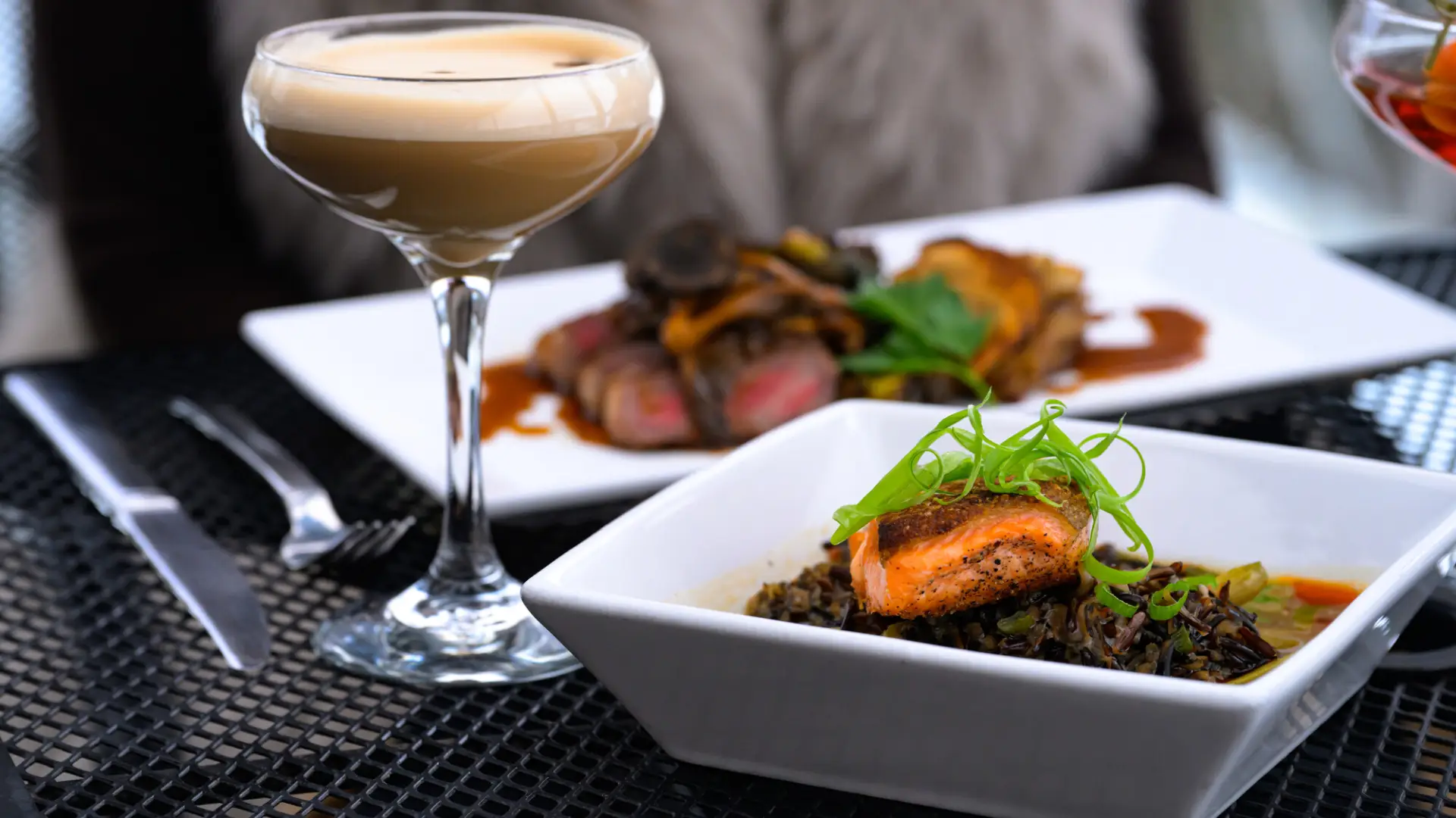 An espresso martini and a plate of salmon and rice on a table. 