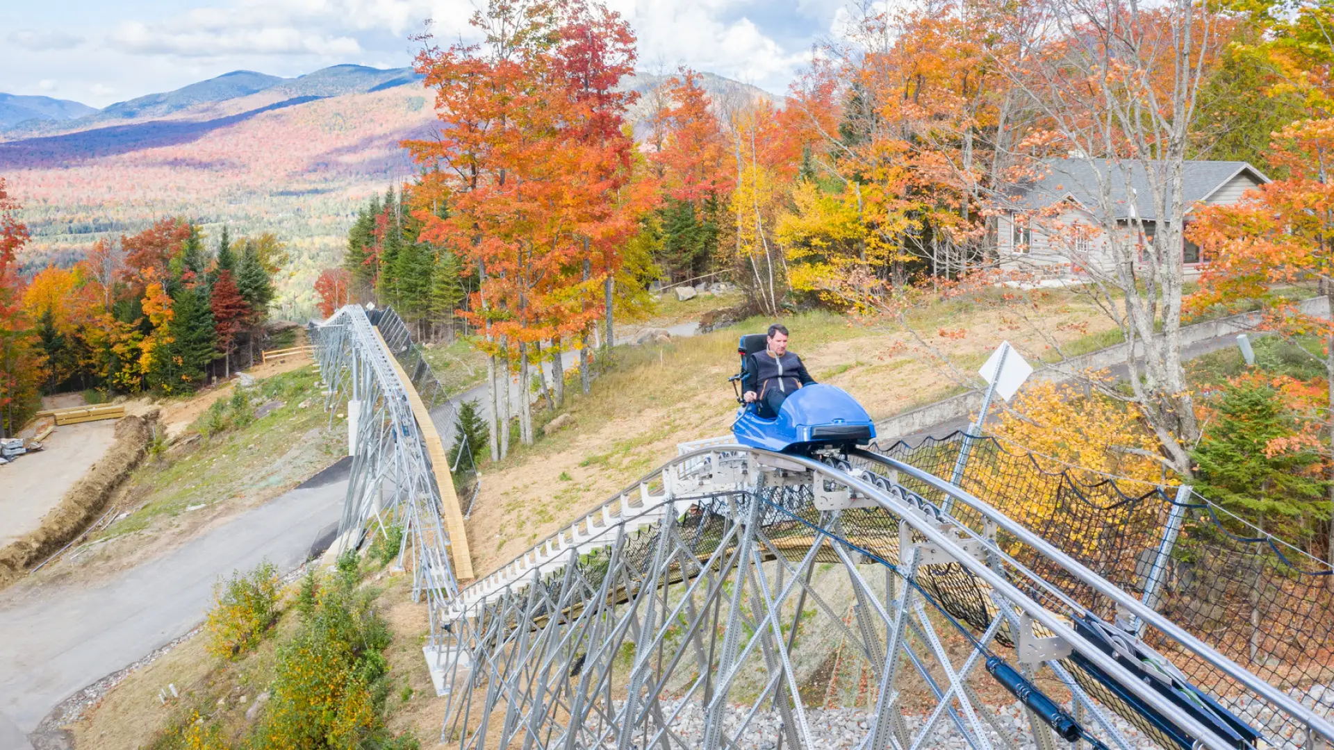 Man rides mountain roller coaster with fall foliage and mountains in background