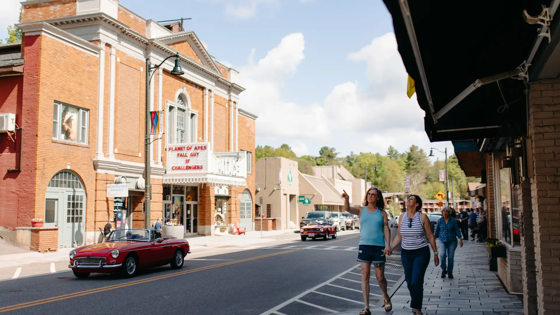 A charming, retro downtown in a small town. People on the sidewalk point into the distance.