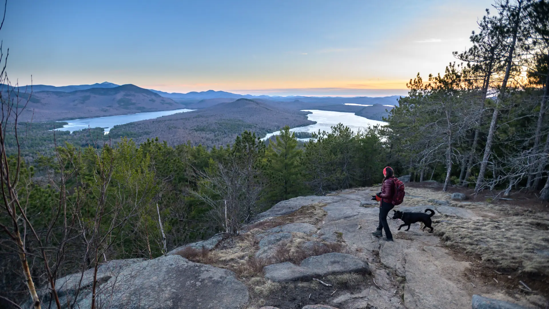 A hiker and her dog standing at the summit of a hike during the spring.