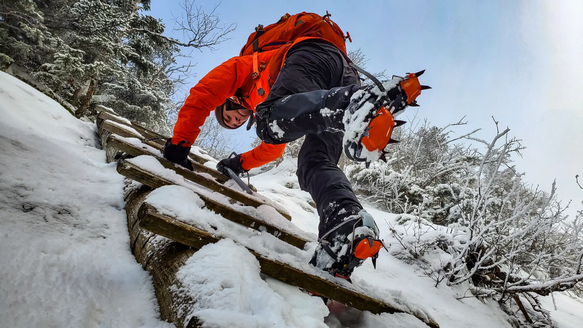 A hiker in crampons going down a ladder in the winter.