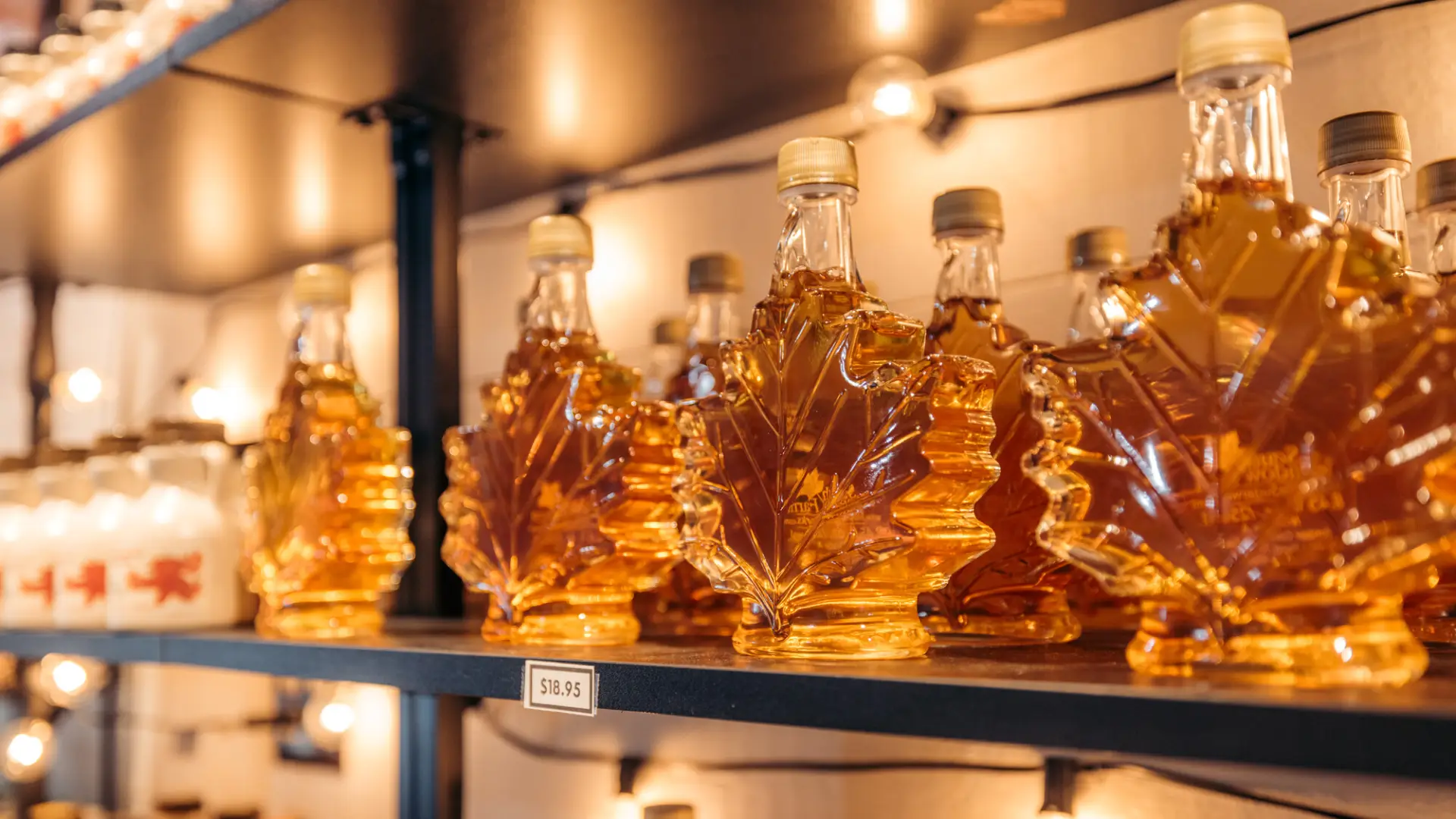 Glass maple leaf jars on shelf filled with golden maple syrup