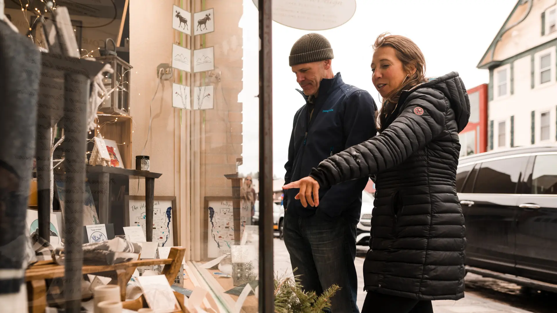 A man and woman in winter coats window shop. 