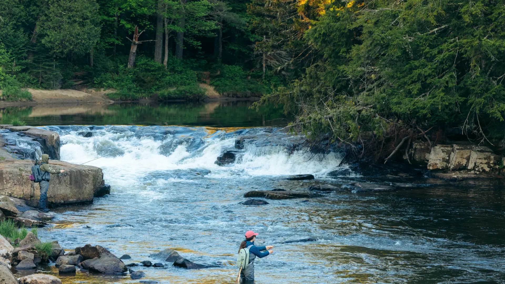 A fly fisher near a short waterfall