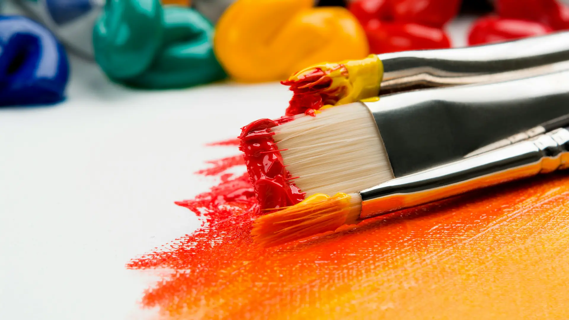Stock image of paint globs on canvas with reds and oranges painted and paint brushes covered in paint.