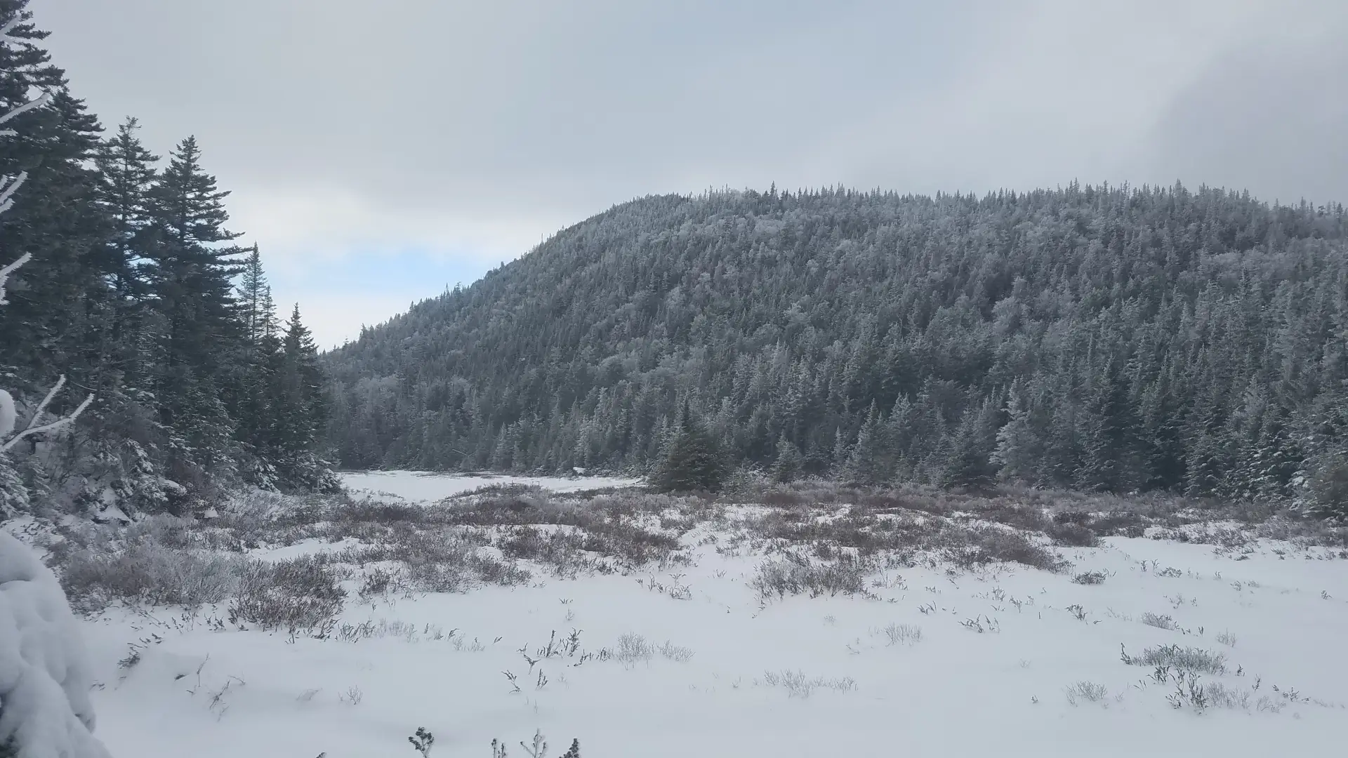 The view of a snowy ridge across a frozen pond