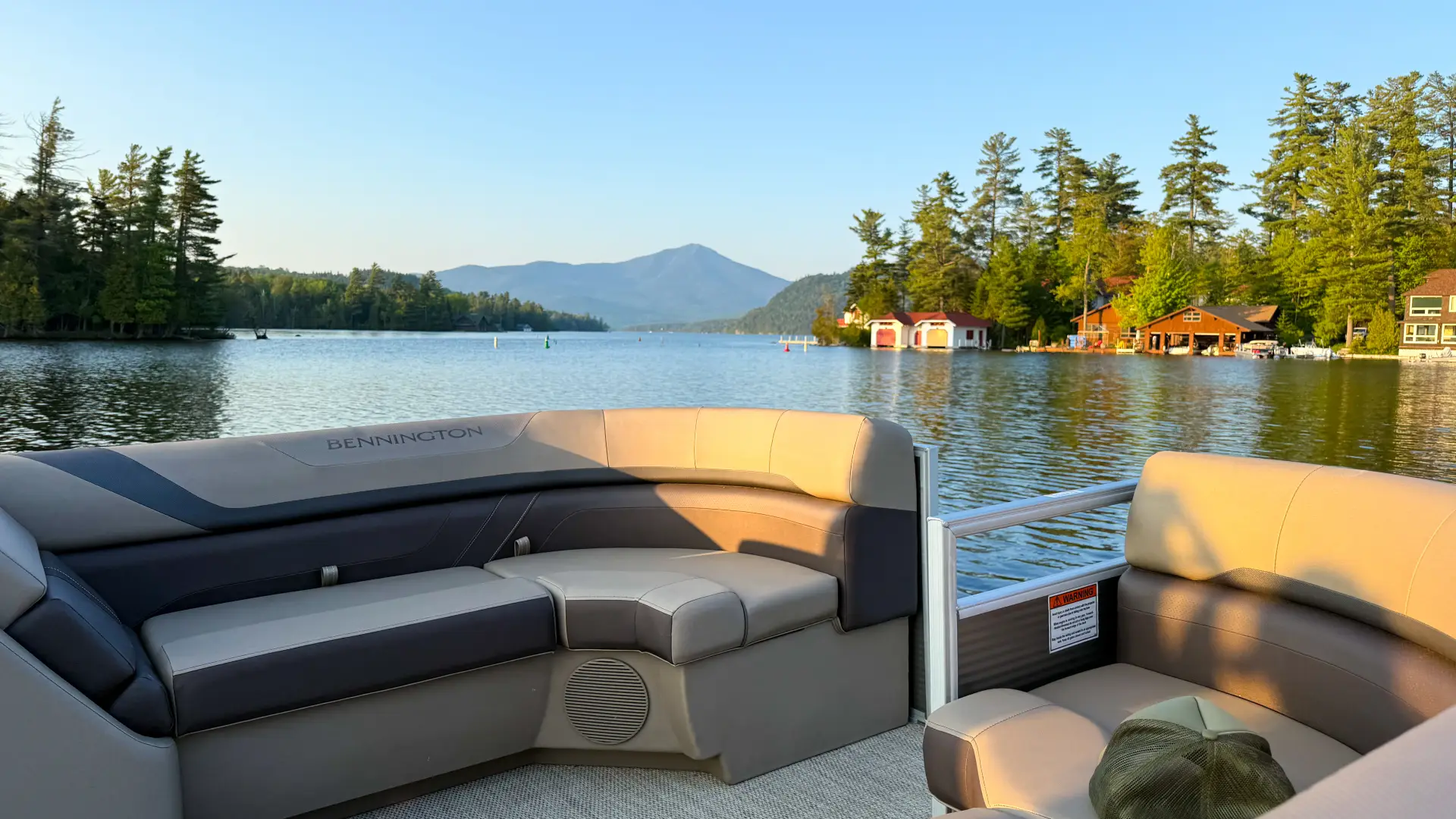 The seats of the back of a pontoon boat with glassy lake water and a misty mountain in the distance