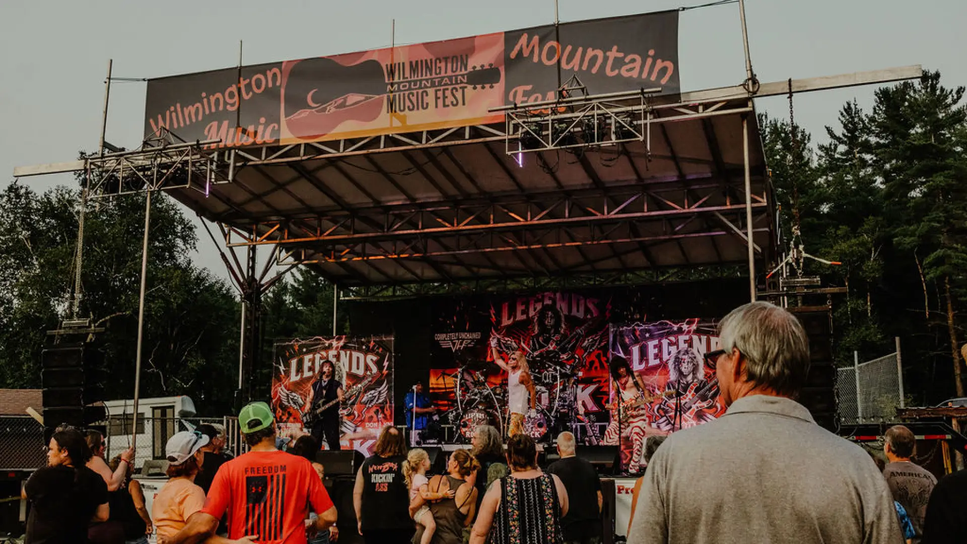 Crowd of people stands looking at music festival stage outdoors in summer
