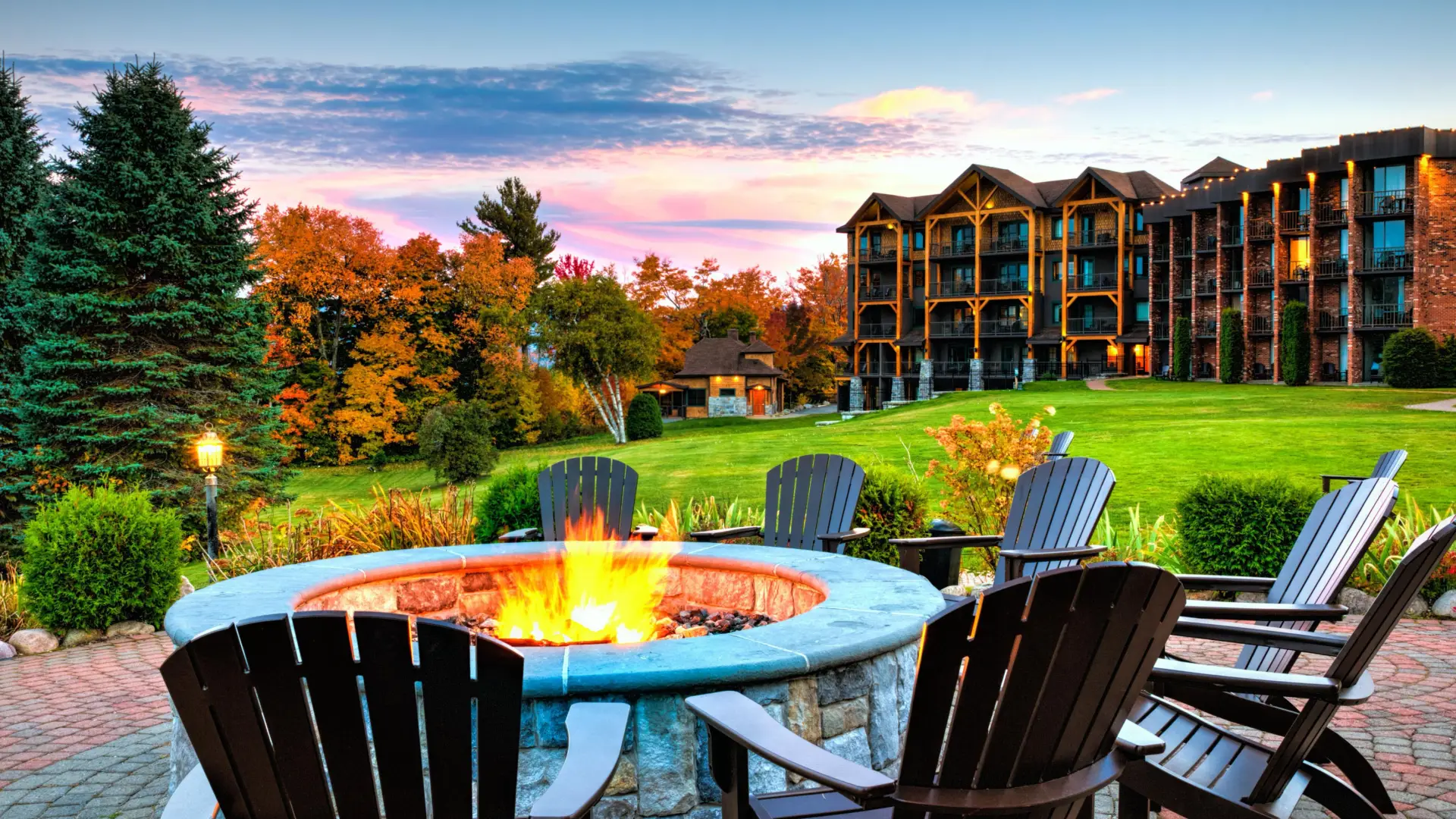 A stone fire pit ringed with adirondack chairs in the front lawn of Lake Placid Club Grandview