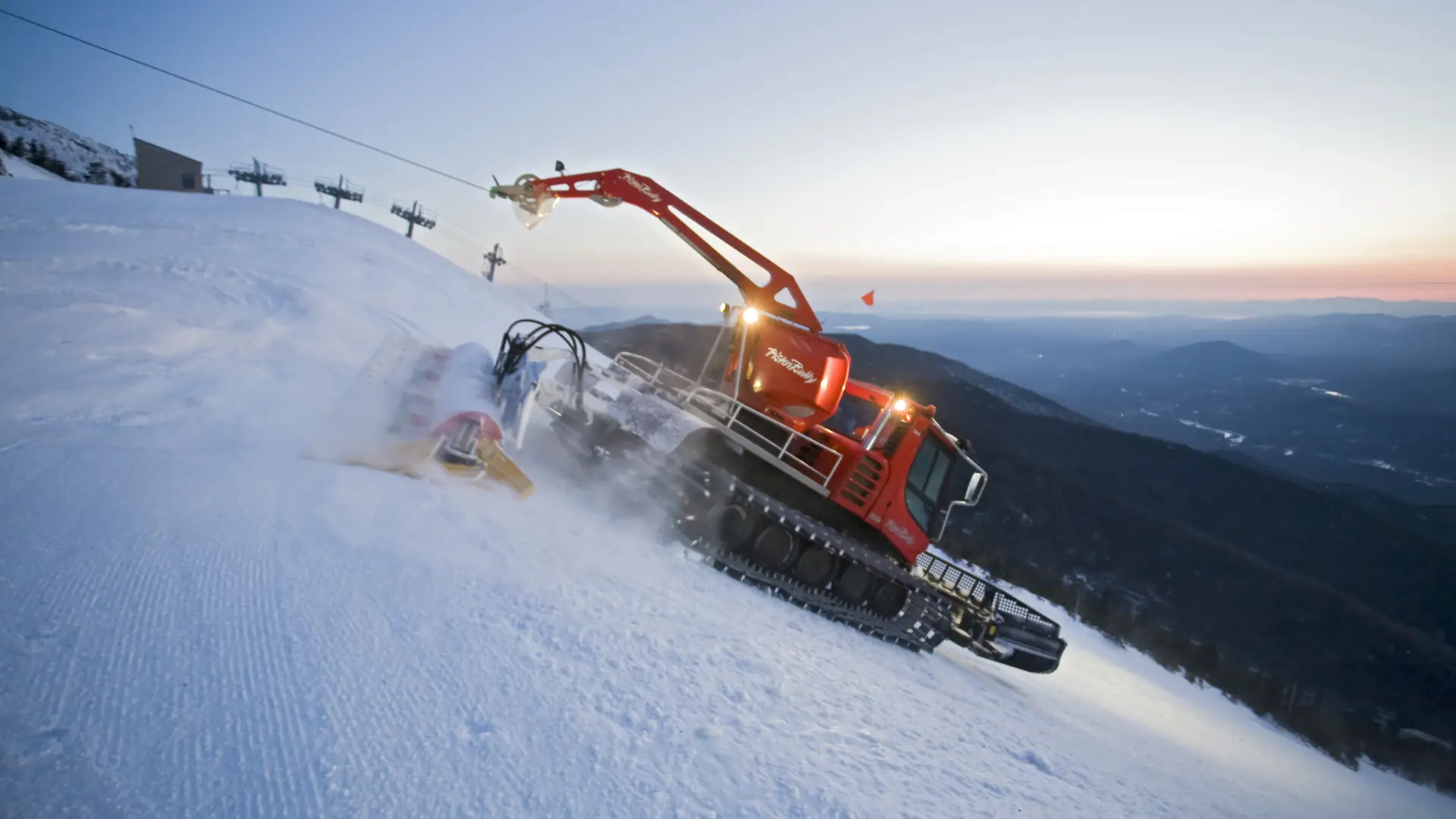 A large snow-grooming machine works its way down a snowy mountain.