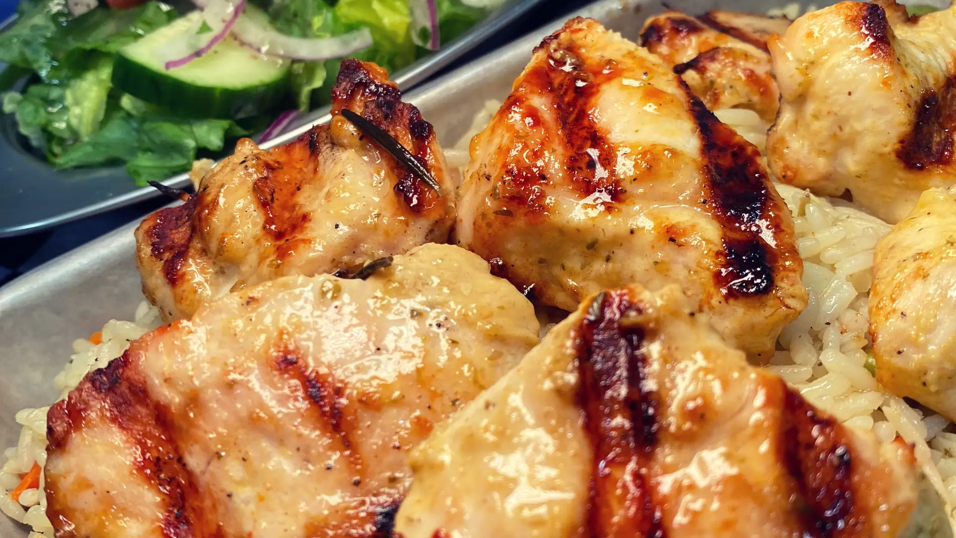 Rice topped with grilled chicken with a fresh salad behind.