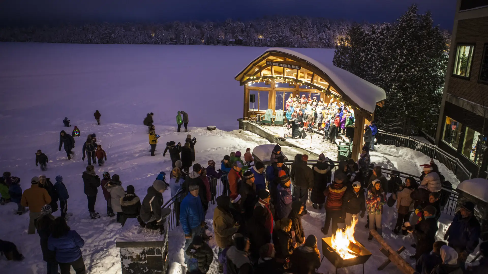 A winter concert on Mirror Lake in Lake Placid with a snowy backdrop and a crowd of people.