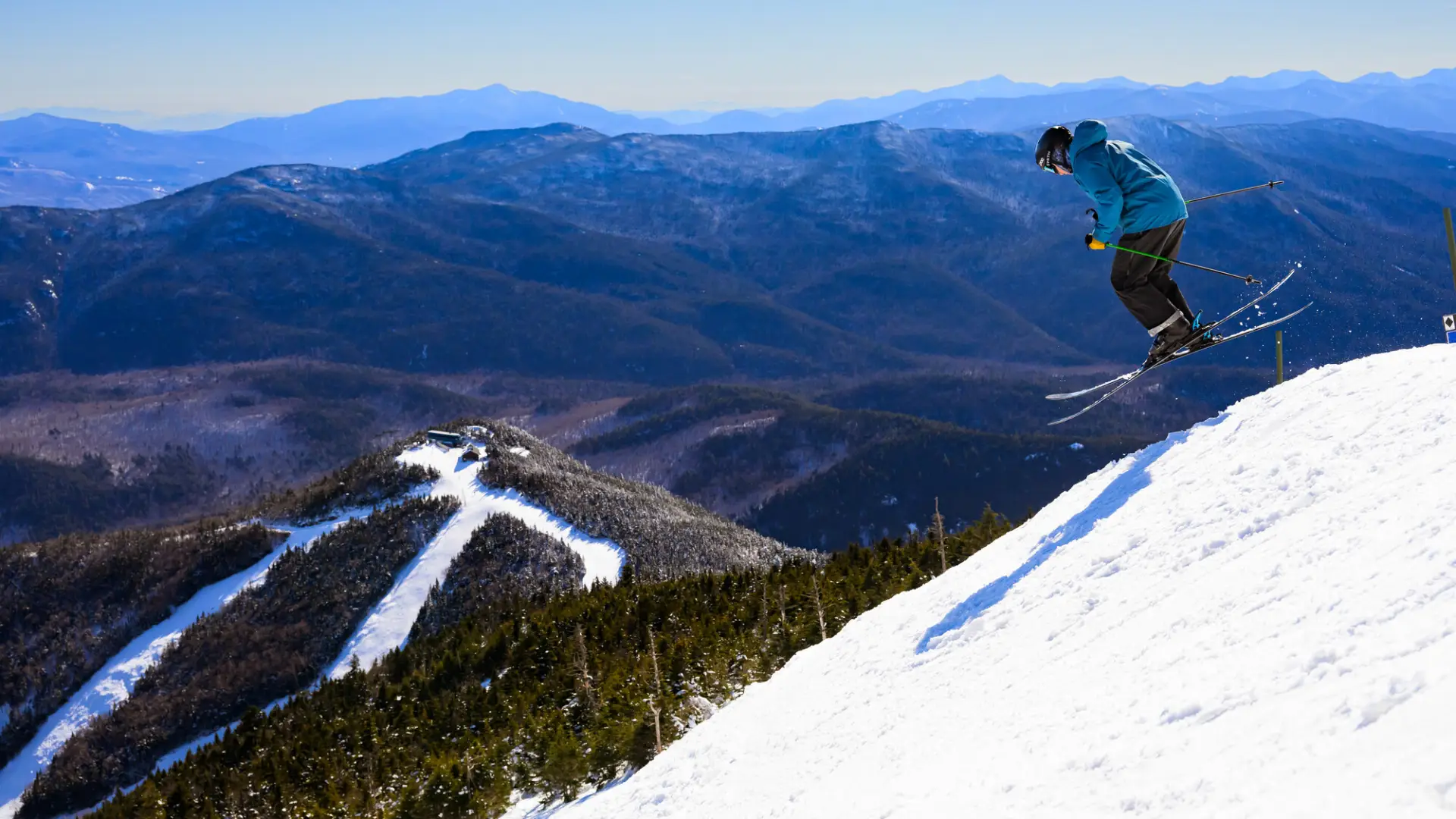 A skier jumps over a snowy hill on top of a mountain.