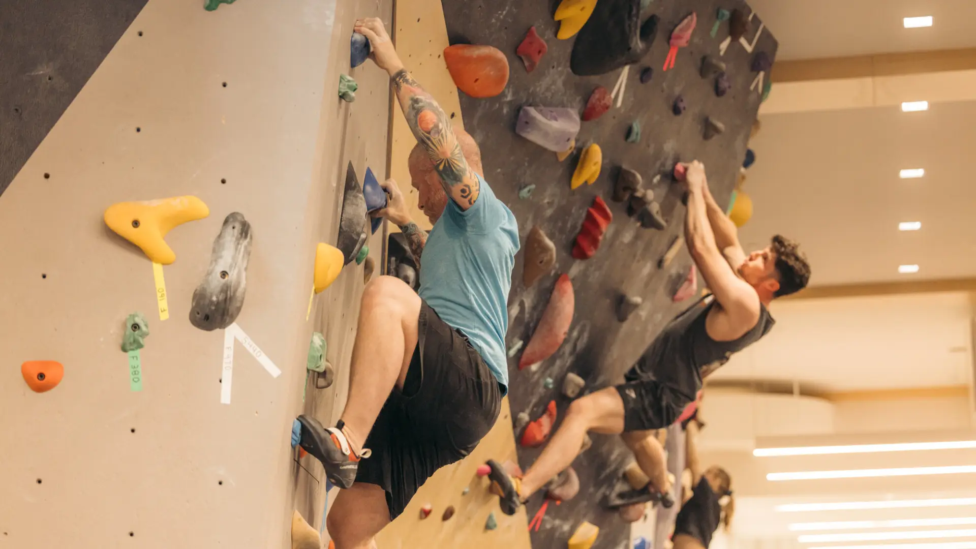 Two climbers seen side by side on indoor bouldering wall