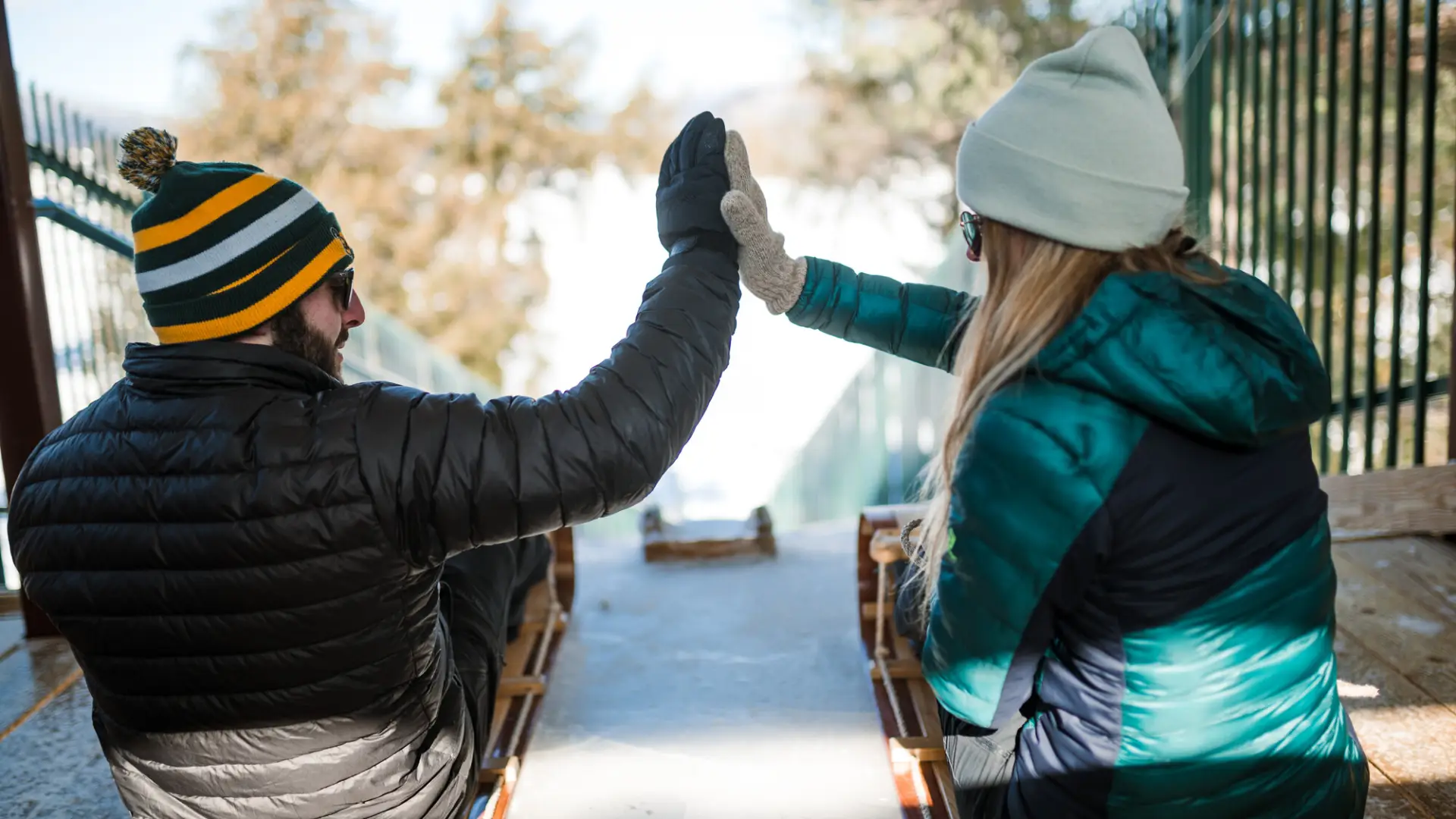 A man and woman high five riding toboggans.