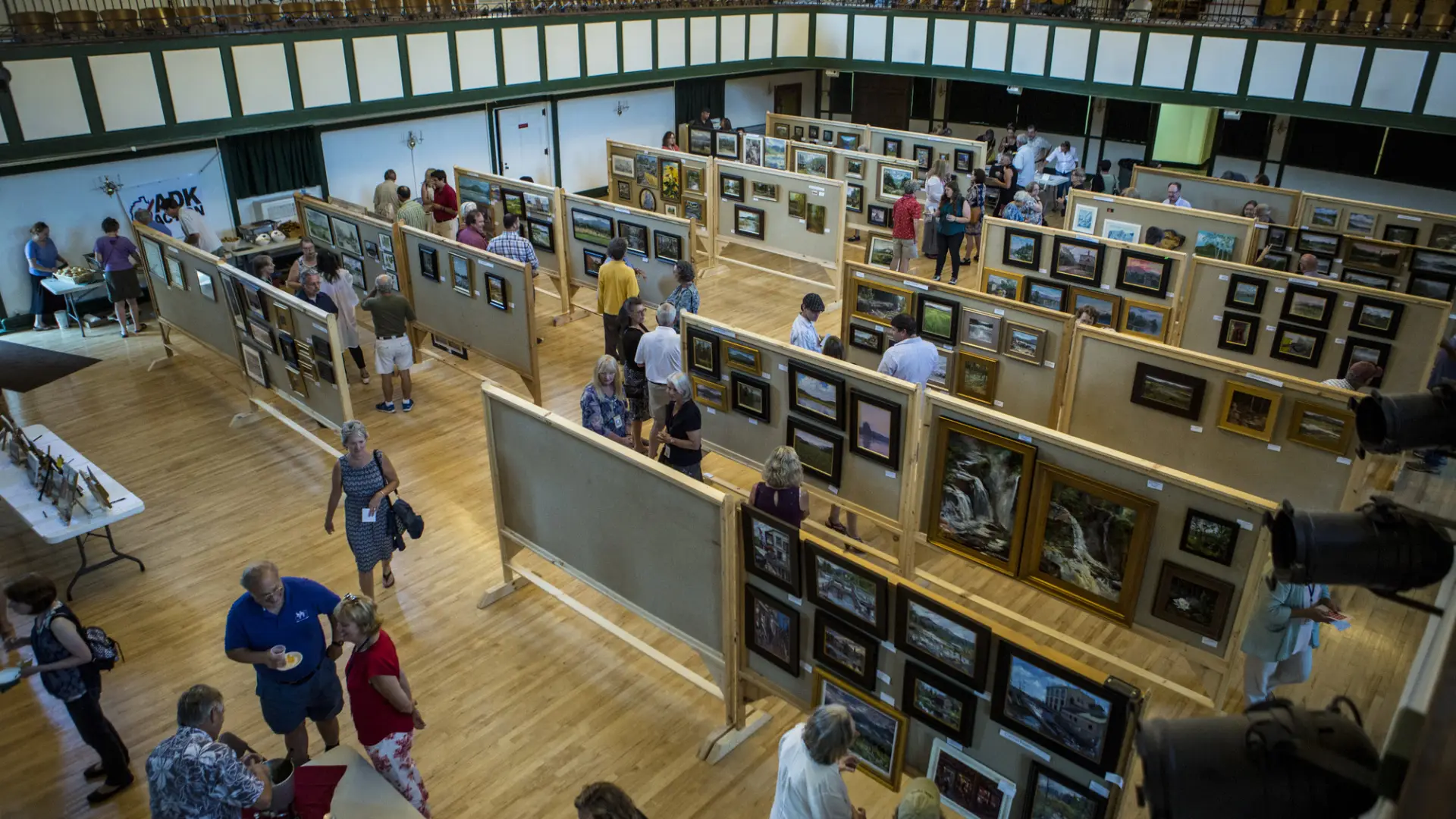 A high-angle view shows a crowd of people browsing an indoor art exhibition.