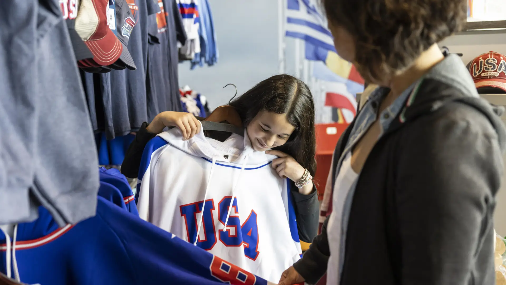 A young woman holds a USA hockey jersey up to herself in a brightly colored shop.