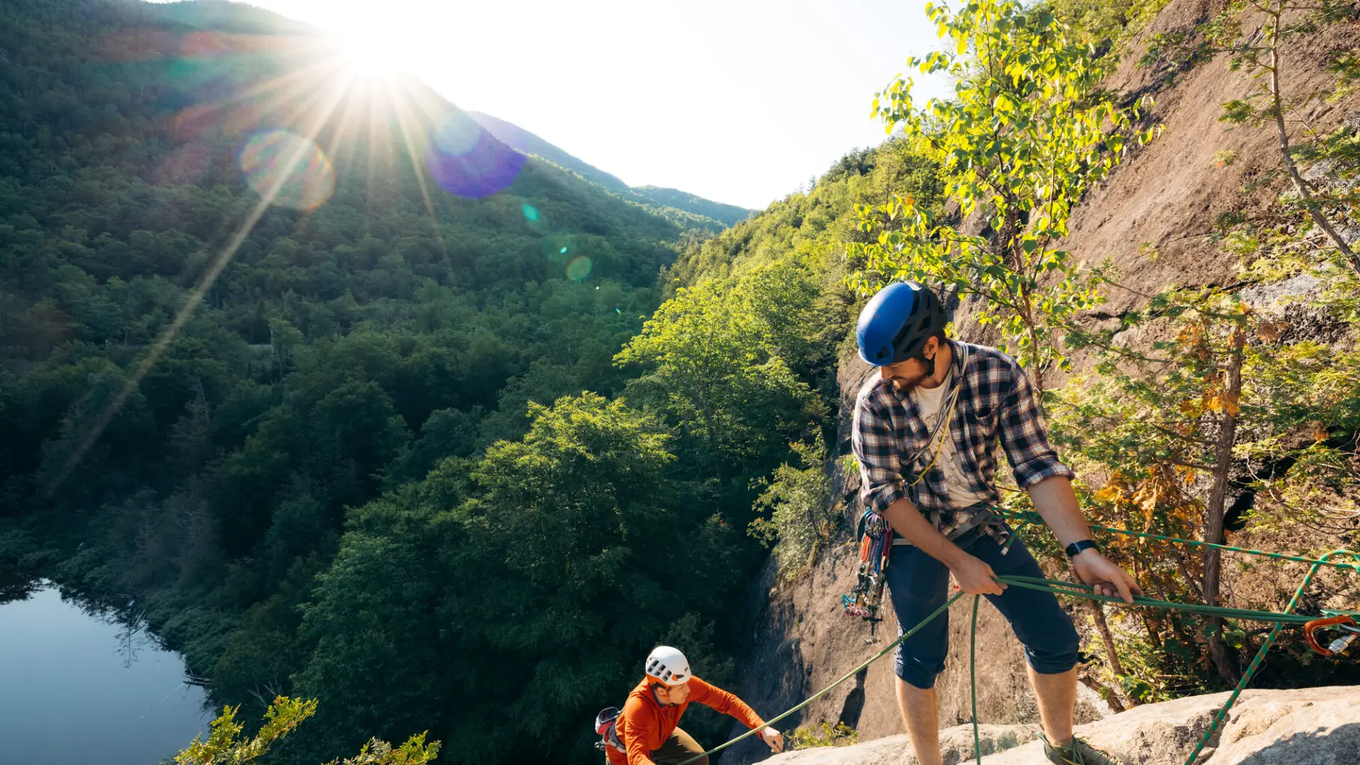two people rock climb up a green mountain. 