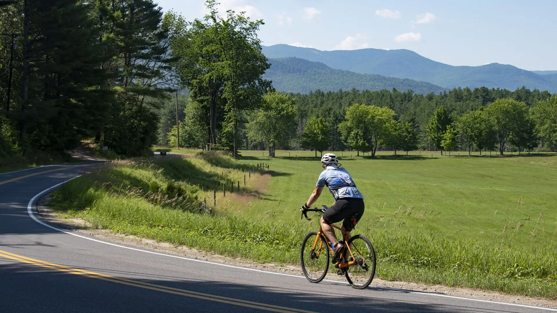 Cyclist on country road with mountain range in background