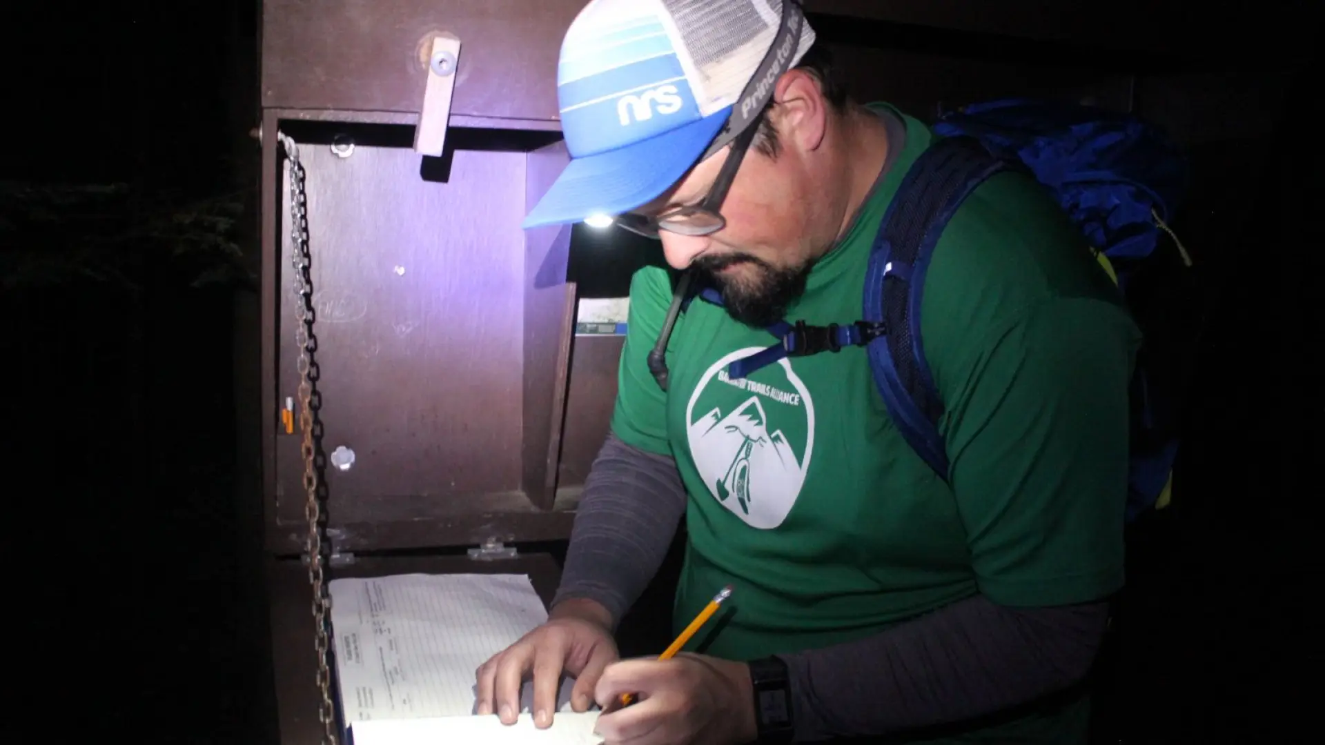 Dan signs the trail register by the light of his headlamp.